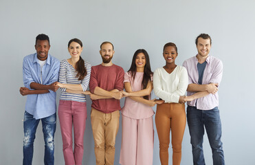 Studio group portrait of happy young diverse friends. Smiling millennial mixed race people holding hands and looking at camera standing isolated on light background. Community and support concept
