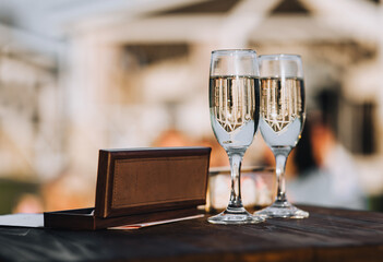Two glasses with alcohol, champagne and a brown fabric cover stand on a wooden table at the ceremony, wedding.