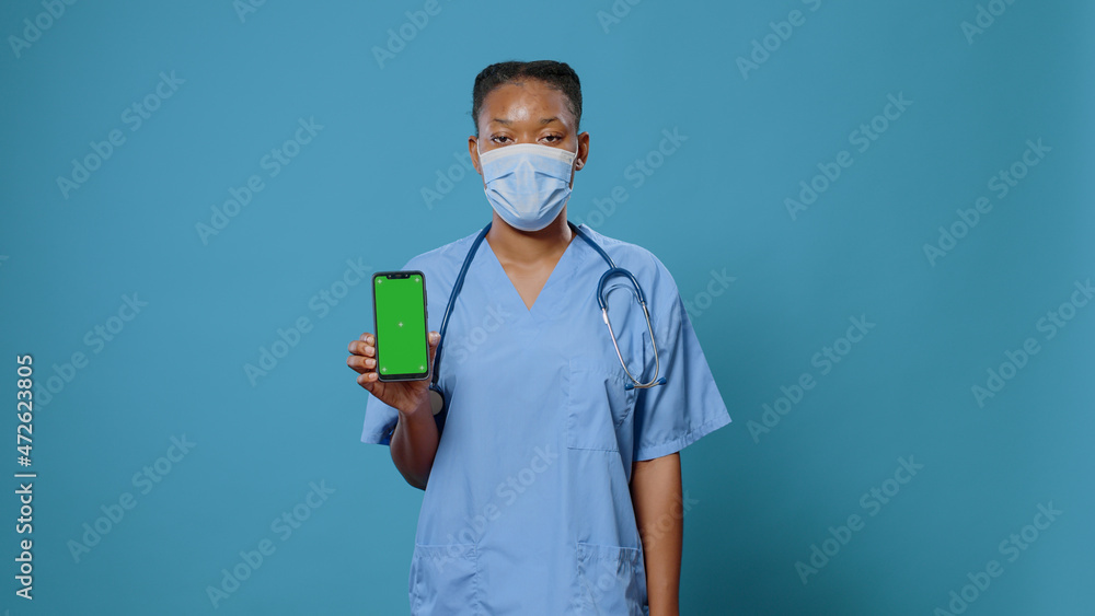 Poster medical assistant vertically holding smartphone with green screen and looking at camera. nurse with 