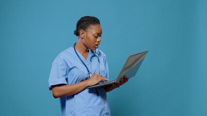 Portrait of medical nurse in uniform looking at laptop display to work on healthcare system and...