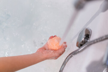 Beautiful woman holding an aromatic orange bath bomb on her hands before put it into the bathtub. 