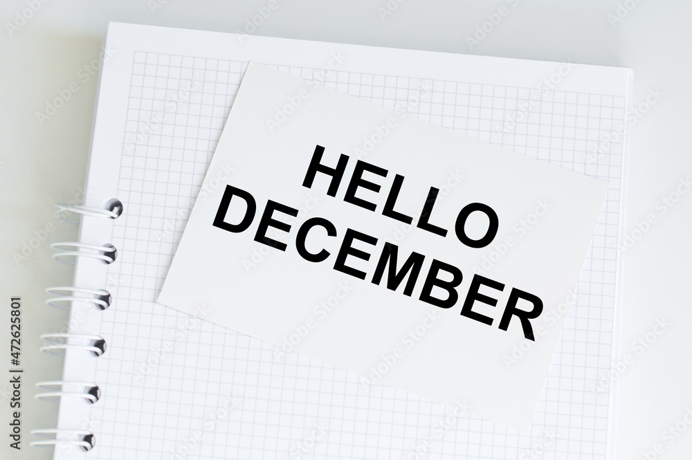 Poster hello december text on a card that lies on a notebook on a light table, business concept