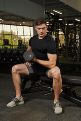 Fototapeta na wymiar young man shakes biceps with a dumbbell in the gym