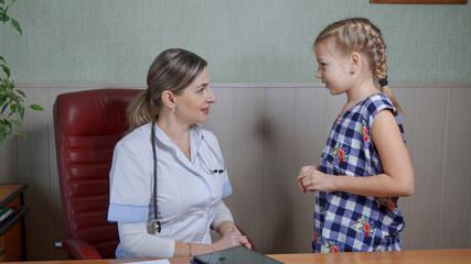 A woman, a pediatrician, examines a girl patient. She makes an analysis of the girl's health and speaks to her affably.
