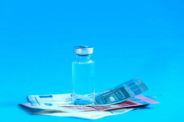 Covid 19 vaccina cost concept. Glass vial and piggy bank stands on blue background.