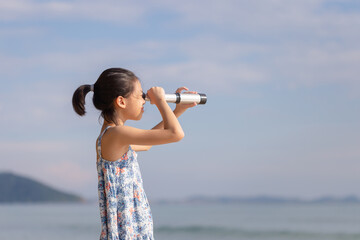 Happy kid playing outdoors on the beach, Asian child girl looking in spyglass - obrazy, fototapety, plakaty