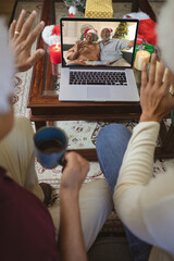 Two waving men making laptop christmas video call with happy african american senior couple