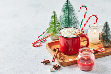 Red cup of hot cocoa with marshmallows and candy canes on with christmas tree
