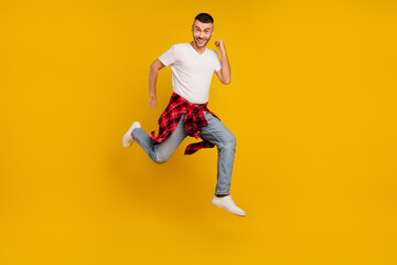 Fototapeta na wymiar Full size photo of young happy man jump up runner wear checkered shirt tied on waist isolated on yellow color background