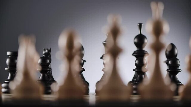 Close-up of chessboard with lines of white and black wooden chess figures ready to play with blurred foreground and background