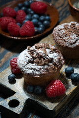 chocolate muffins and fresh berries on wooden board, top view