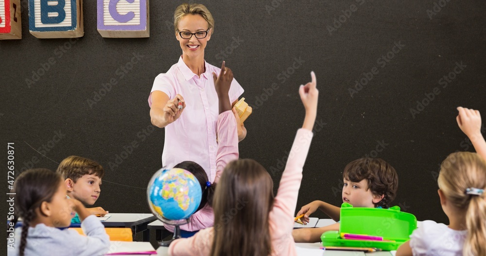 Poster smiling teacher pointing at students with hands raised while teaching in classroom