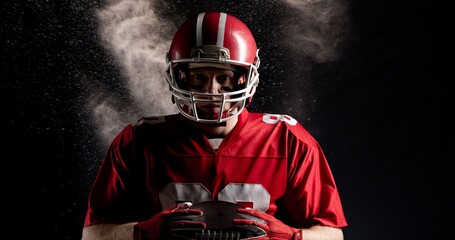 Digital composite of american football player holding ball against black background with smoke