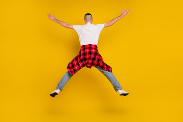 Fototapeta na wymiar Full length photo of young man jump up raise hands star shape checkered shirt tied on waist isolated on yellow color background