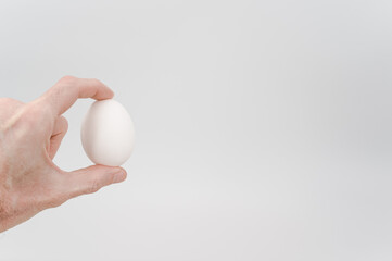 Fototapeta na wymiar white egg in a male hand on a white background with text space