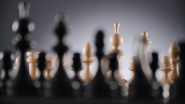 Close-up of rotating chessboard with lines of white and black wooden chess figures ready to play with blurred foreground and background