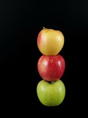 A tower of three apples of different colors. Green, yellow and red apple on a black background.