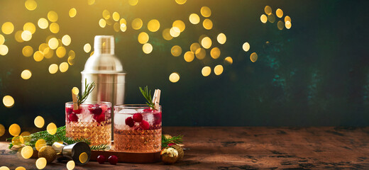 Alcoholic cocktail or non-alcoholic cocktail with vodka and cranberries with ice, shaker, jigger and bar spoon, fir branches and glowing garland for christmas on wooden background