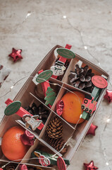 Basket with wooden clothespins with figures train,angel,Christmas tree,snowman,Santa Claus with the words Merry Christmas on German language;cones,walnut,tangerines,stars and a garland lights top view