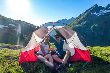 A couple camping in a wilderness. They sit in a small tent, placed on a top of a mountain peak,...