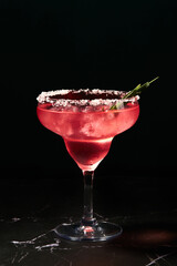 Alcoholic or non-alcoholic rosemary cocktail such as margarita, cosmopolitan or similar on a dark marble table