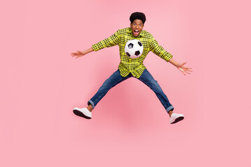 Full size photo of young cool brunette guy jump with ball wear shirt jeans sneakers isolated on pink background