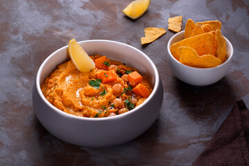 Hummus with sweet potato, chickpea, tahini, garlic and olive oil topped with lemon slice, herbs and sumac. Middle Eastern cuisine meal. Nachos in the background