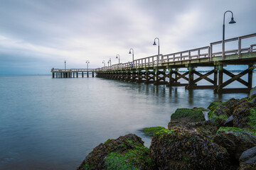 Dramatic seascape with a long commercial pier with lamps and seaweed-covered rocks in New Haven Harbor, Connecticut.