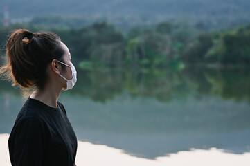 Side view point of young woman wear protection mask beside the lake and her look at faraway , hope and dream concept