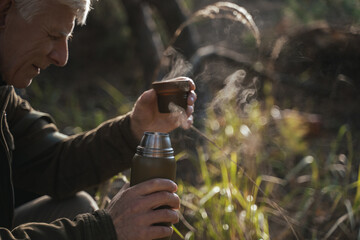 Elderly male person holding cup with hot beverage with kind smile