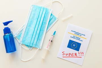 Covid Green Pass with text "super", blue mask, hand sanitizer, and syringe labeled "vaccine booster dose" on a white surface. Introduction of the super green pass and third dose of the vaccine, or boo