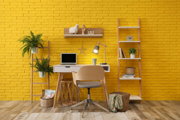 Modern workplace interior with wooden furniture and laptop near yellow brick wall