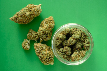 Close up of cbd cannabis buds in glass jar, macro view. Medicinal marijuana blooms on green paper...