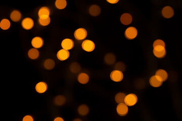 Defocused bokeh lights on black background, an abstract naturally blurred backdrop for Christmas eve or birthday party. Festive light texture. Yellow and red garland in blur. Overlay effect for design