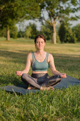 Young woman meditates in the park in the lotus position at sunset. Yoga classes in nature