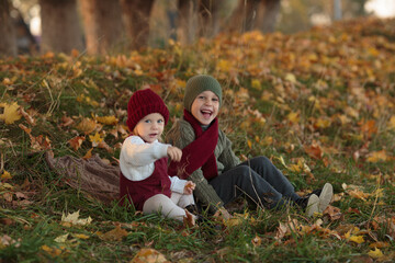 Fototapeta premium brother and sister are sitting together and laughing, the boy is wearing a green knitted hat, a green sweater, a red scarf, and the girl is wearing a white knitted sweater, a red sundress, a red hat a