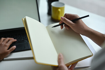 Top view of a woman hands taking notes over the white blank screen digital tablet with keyboard case as a background.