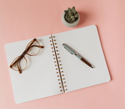 Cahier à spirale ouvert sur une page blanche avec lunettes et stylo - Décor rose avec succulent pour l'inspiration pour l'écriture