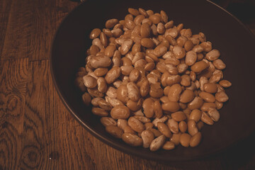 boiled white beans in a dark ceramic bowl on wooden table. Ready for making salad with beans