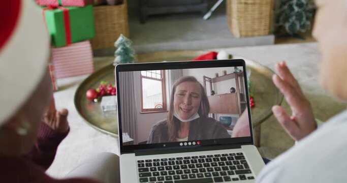 Diverse senior female friends using laptop for christmas video call with happy woman on screen