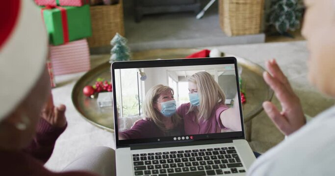 Diverse senior female friends using laptop for christmas video call with happy family on screen