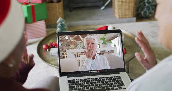 Diverse senior female friends using laptop for christmas video call with happy woman on screen
