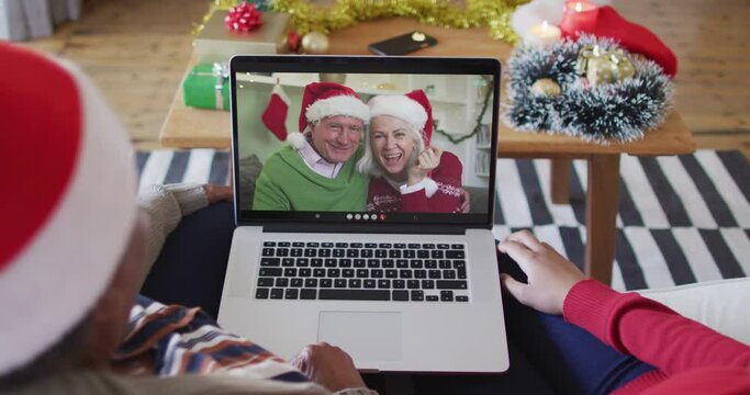 African american mother and daughter using laptop for christmas video call with couple on screen