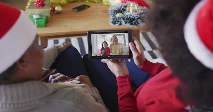 African american mother and daughter using tablet for christmas video call with family on screen