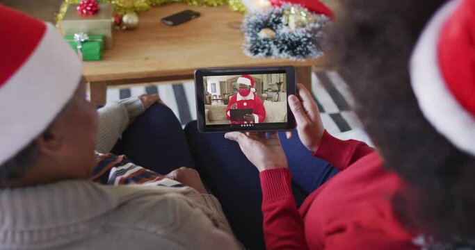 African american mother and daughter using tablet for christmas video call with santa on screen