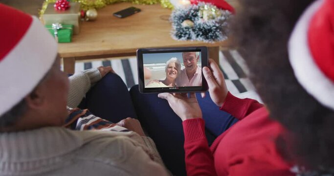 African american mother and daughter using tablet for christmas video call with couple on screen
