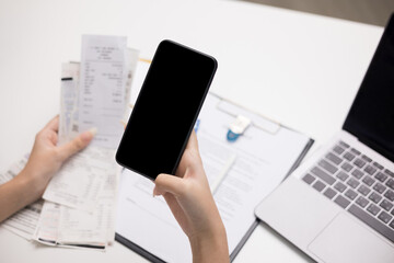 Close up woman is using a smartphone to scan the bill to calculate her income and expenses. In hand there were bills to pay a lot in debt. Purchase with scan qr code payment online.