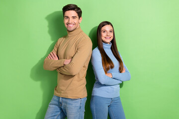 Fototapeta premium Portrait of two positive attractive people stand back to back crossed arms isolated on green color background