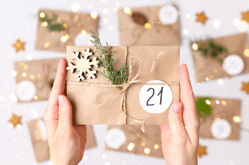 Christmas advent calendar. Woman's hands making gifts with kraft envelopes, fir branches, pine cones. Top view