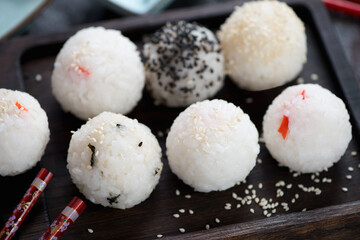 Close-up of onigiri or rice formed into ball shapes on a black wooden serving tray, selective focus